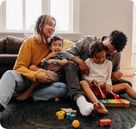 A young family of four play with toys in their living room. 